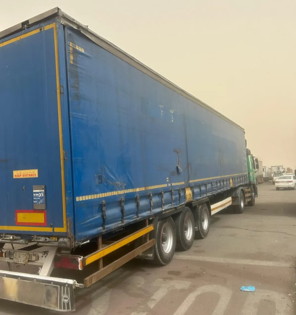شاحنة نقل كبيرة بمقطورة مغطاة باللون الأزرق متوقفة على جانب الطريق، تُستخدم في نقل البضائع لمسافات طويلة