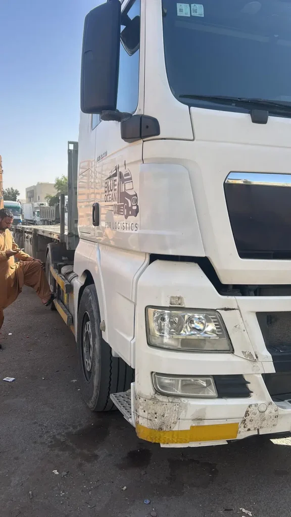 شاحنة نقل بيضاء تابعة لشركة لوجستية متوقفة في الشارع، يظهر جانب الكابينة الأمامي مع شعار الشركة على الباب